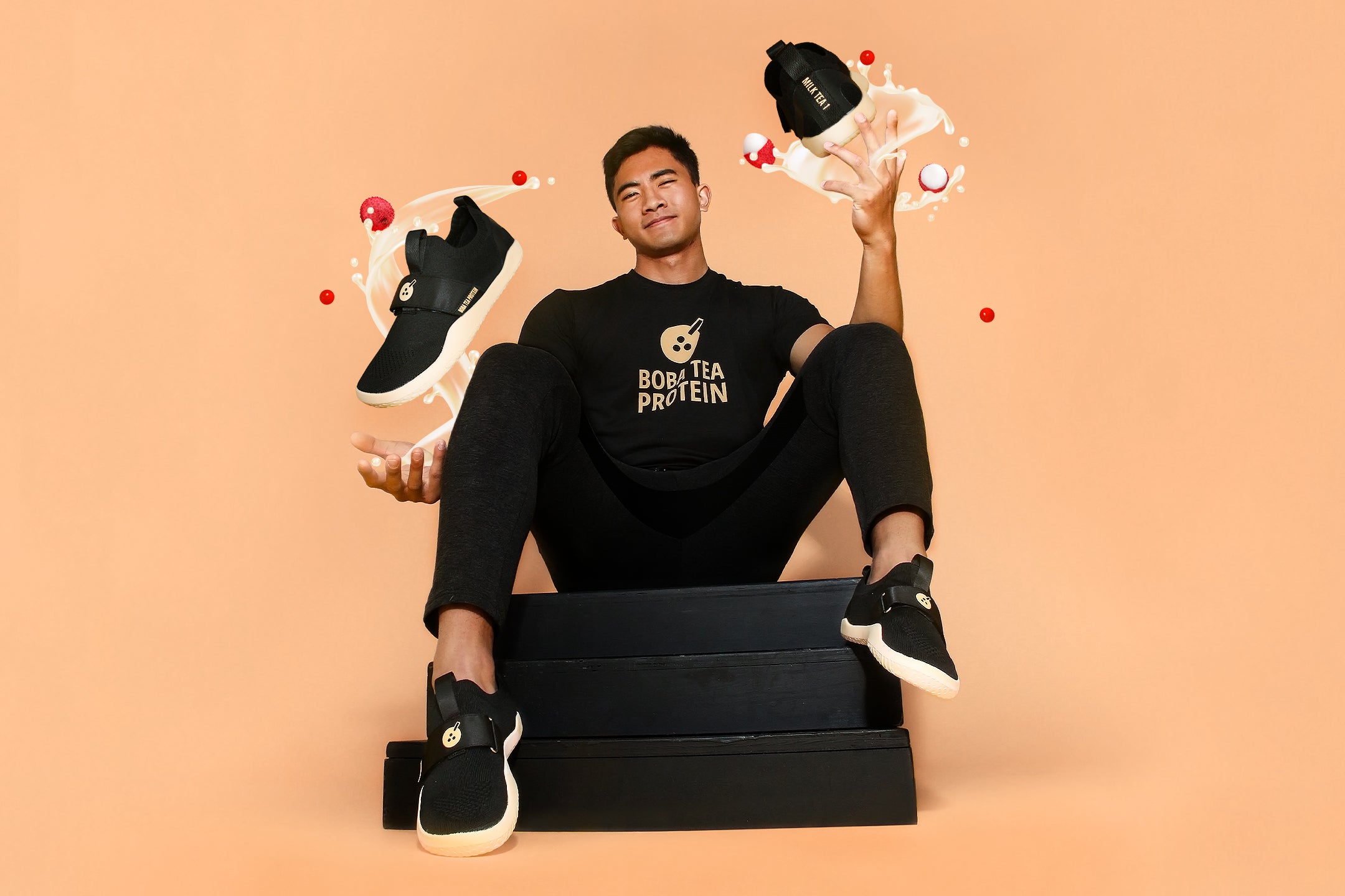 Man in Boba Tea Protein outfit sitting on boxes, tossing branded black sneakers with splash effects.