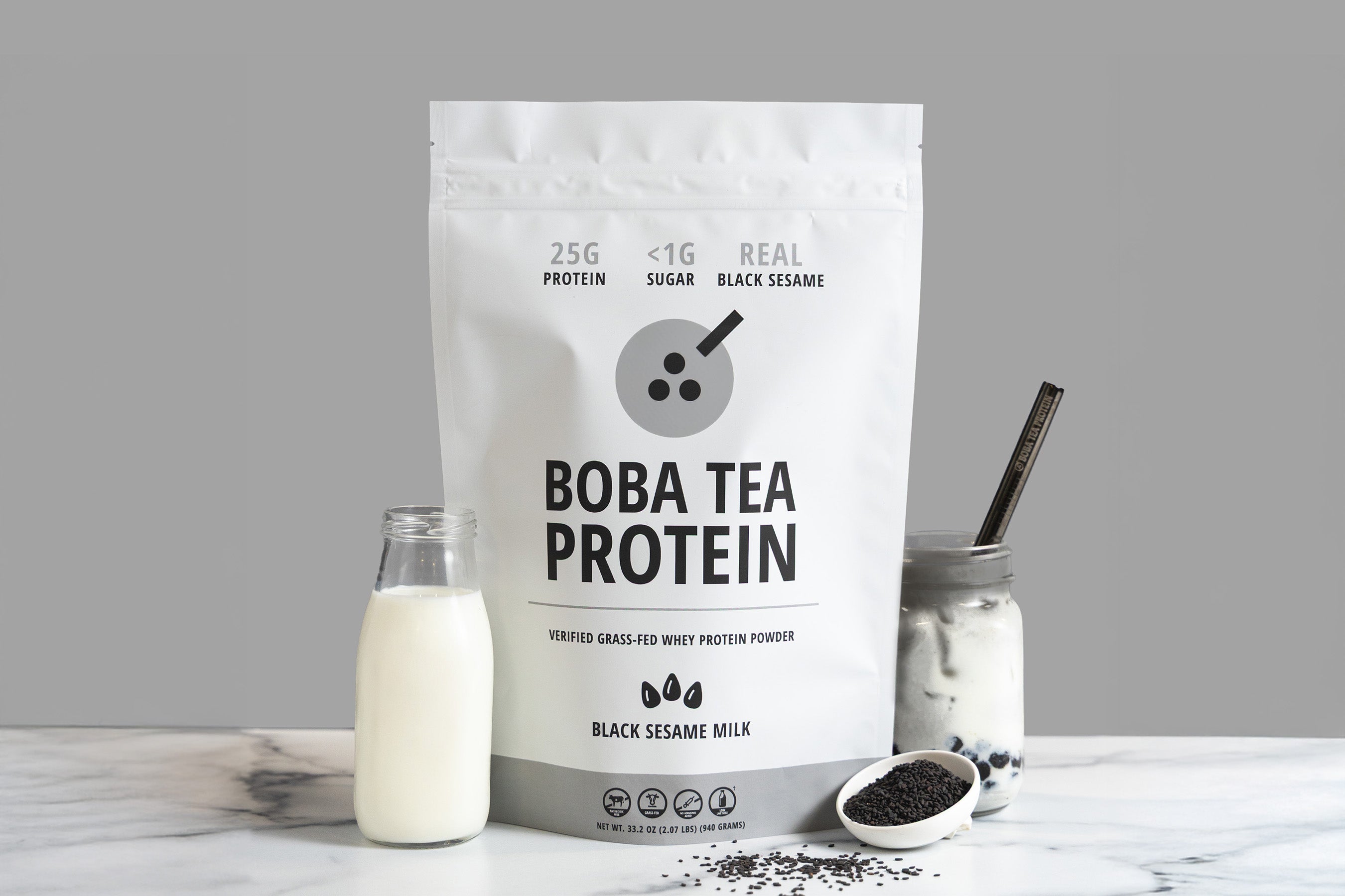 Boba tea protein package with a bottle of milk, black sesame seeds, and a Black Sesame Milk drink on a gray background