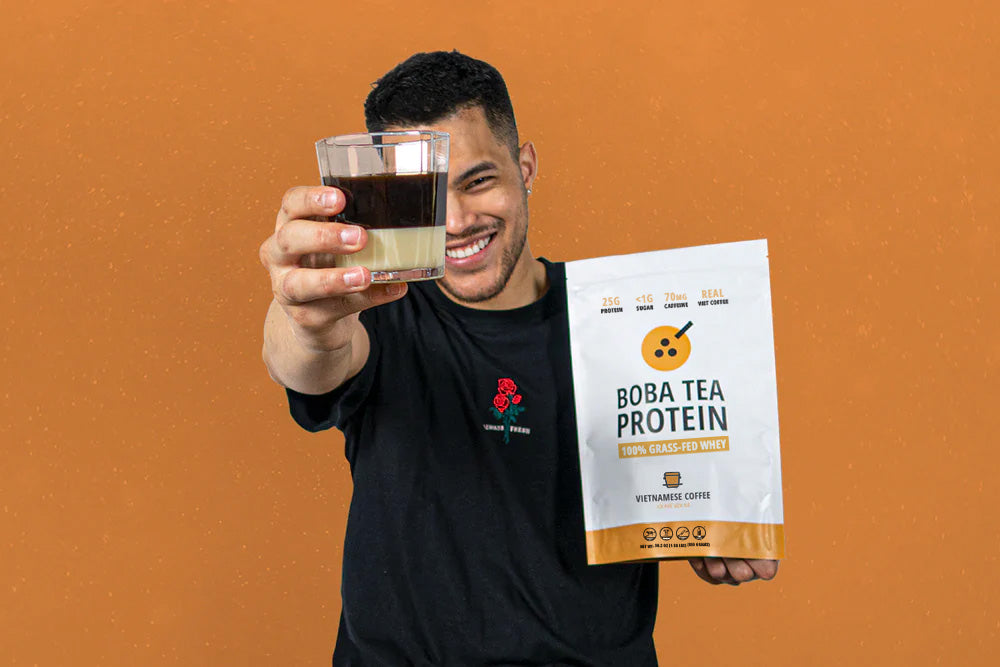Man holding a glass of Boba Tea Protein and its packaging against an orange background