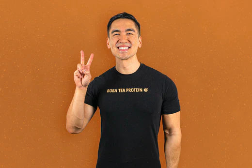 Smiling man wearing a black Boba Tea Protein shirt holding up a peace sign.