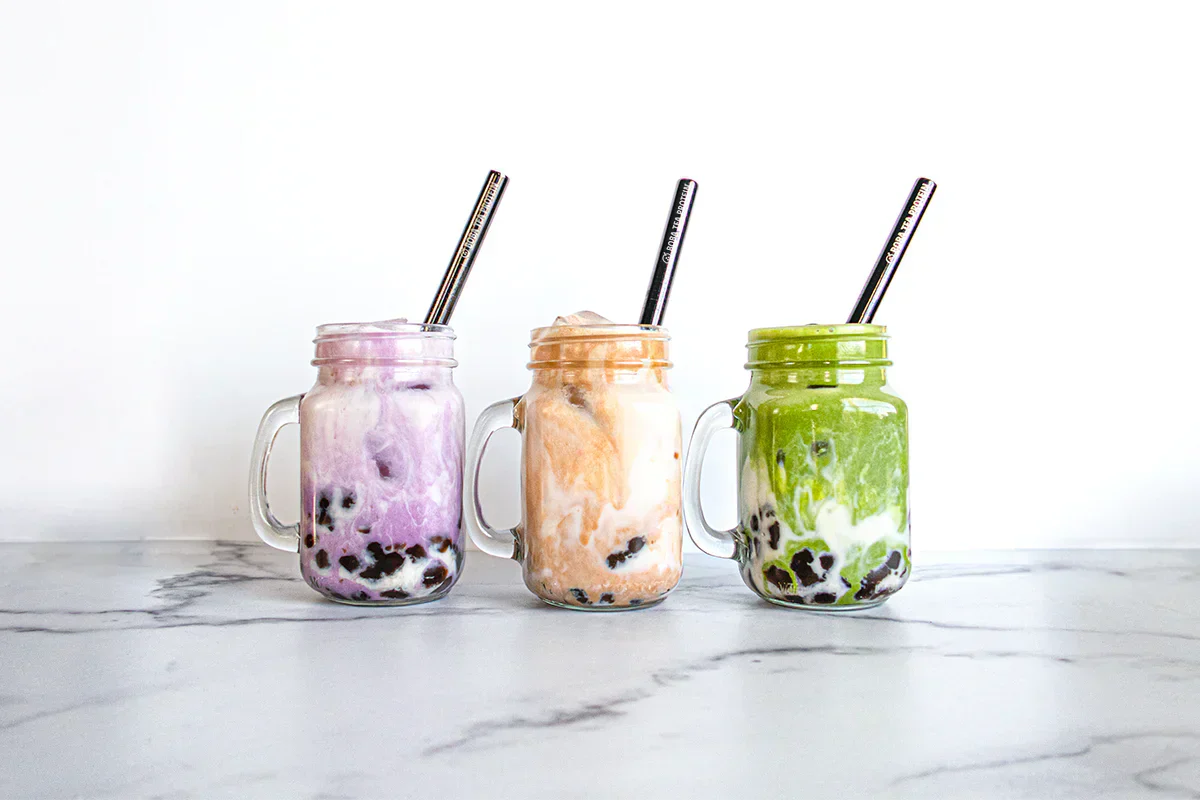 Three colorful boba drinks in mason jars with metal straws on a marble surface.