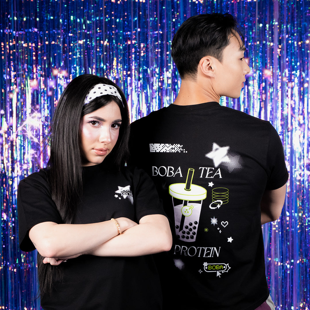 Two people wearing black t-shirts with a Boba Tea Protein design against a colorful curtain background.