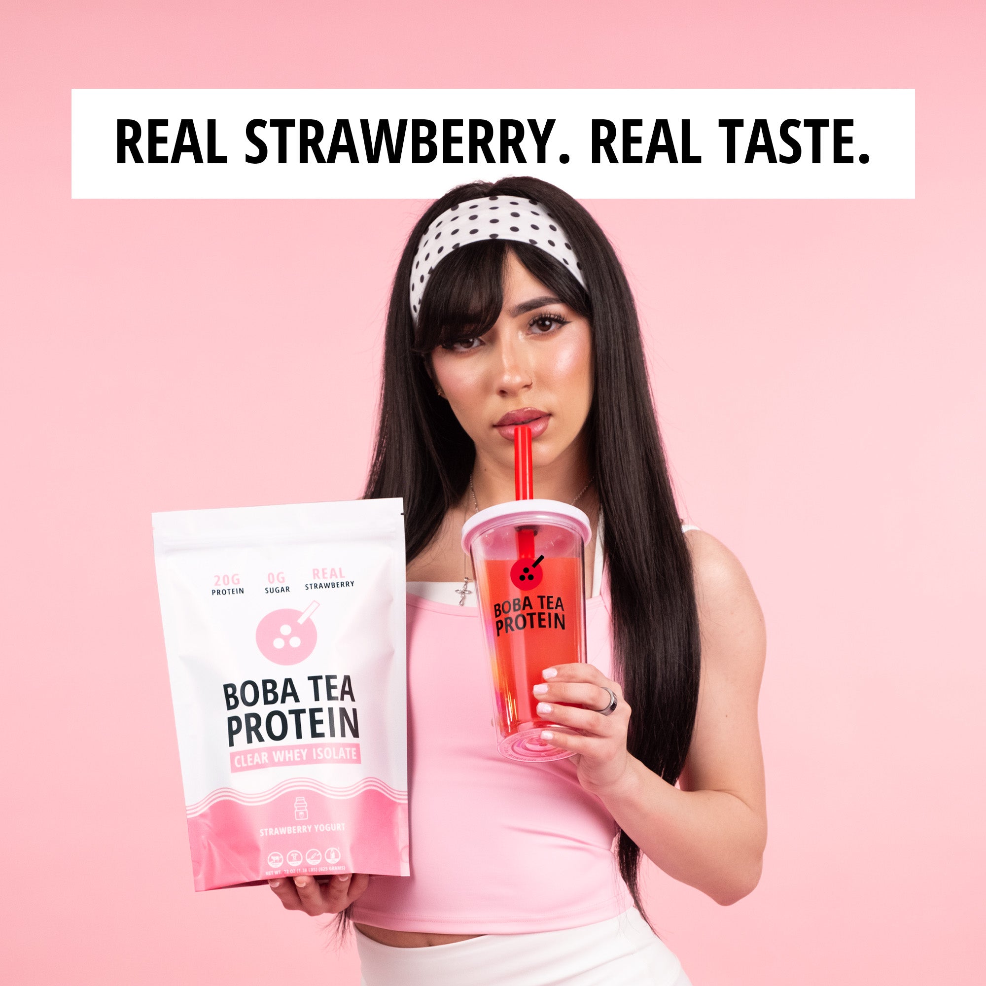 Woman drinking a pink drink and holding a Boba Tea Protein package against a pink background with text that says "real strawberry. real taste."