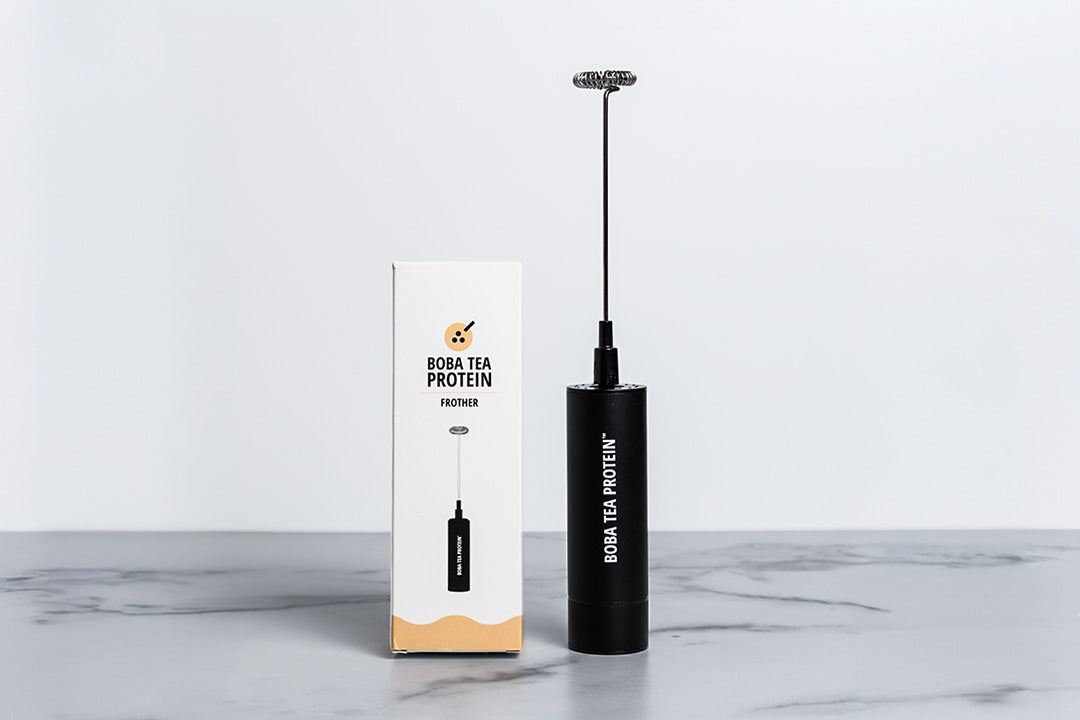 Black handheld milk frother and white box with 'Boba Tea Protein' branding on a marble surface.