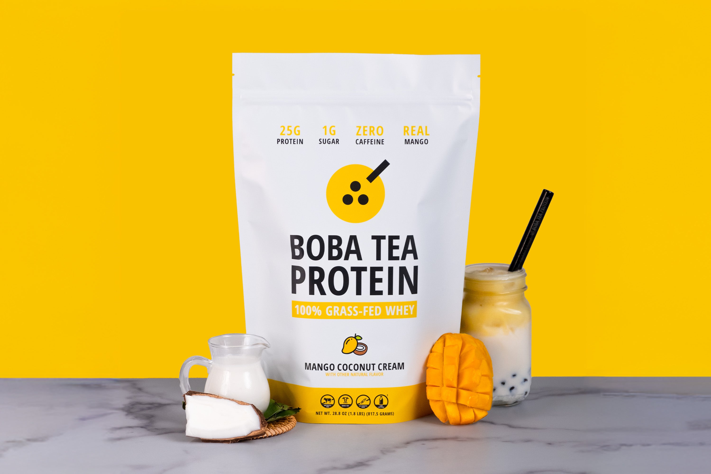 Boba Tea Protein package with a mango coconut cream flavor with mango, coconut, and a drink on a marble surface against a yellow background