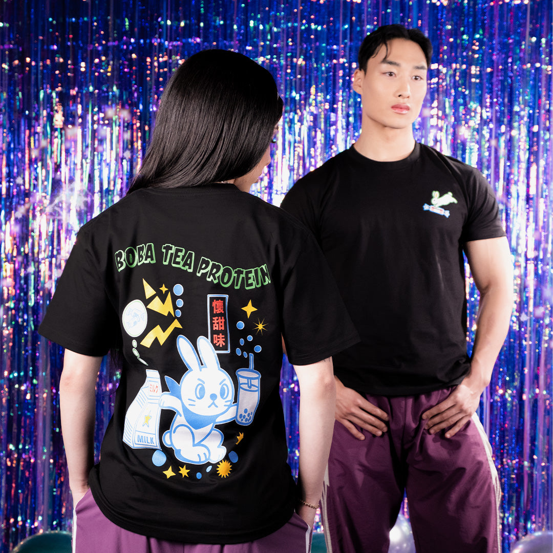 Two people wearing black t-shirts with colorful graphics against a vibrant, multicolored curtain background.