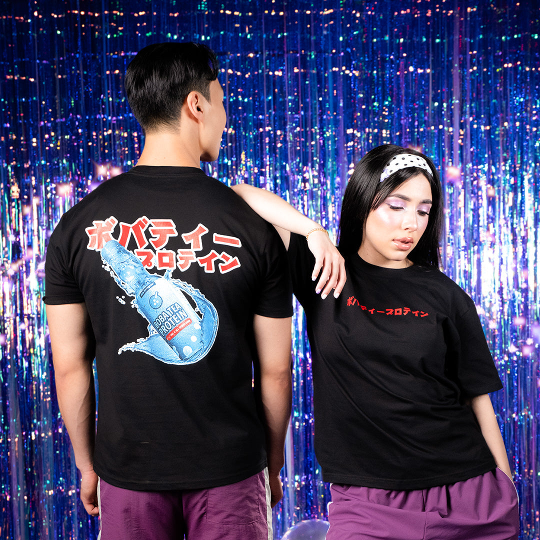 Two people wearing black t-shirts with graphics and text, standing in front of a colorful curtain.