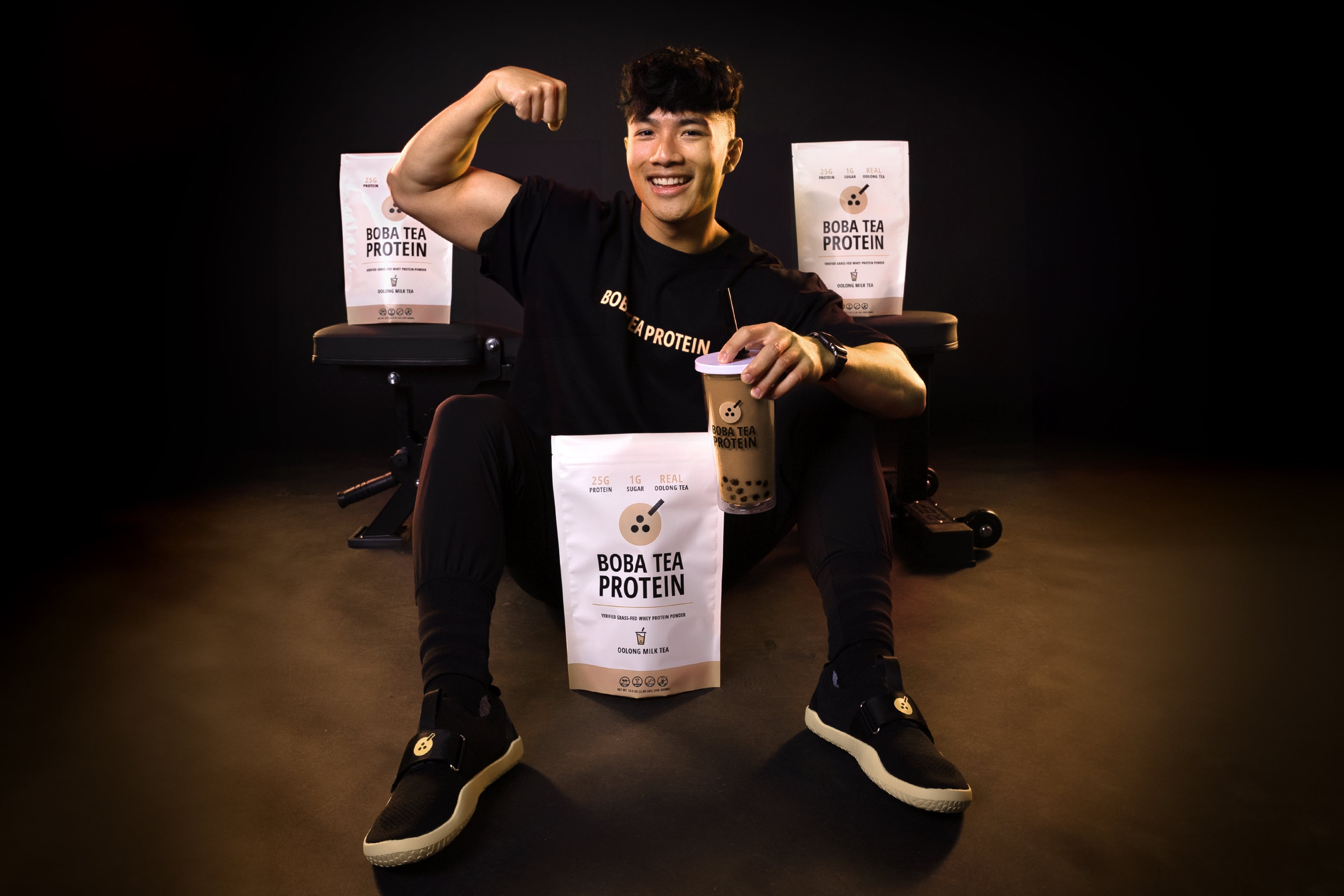 Man flexing muscles with Boba Tea Protein packages in a dark setting